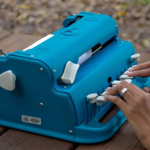 Fotografia de uma pessoa usando uma máquina em Braille azul
